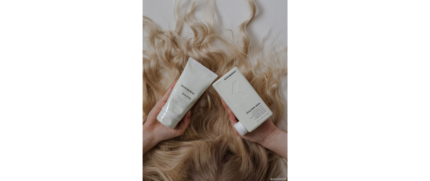 Two bottles of Kevin Murphy scalp care products held over a background of wavy blonde hair.